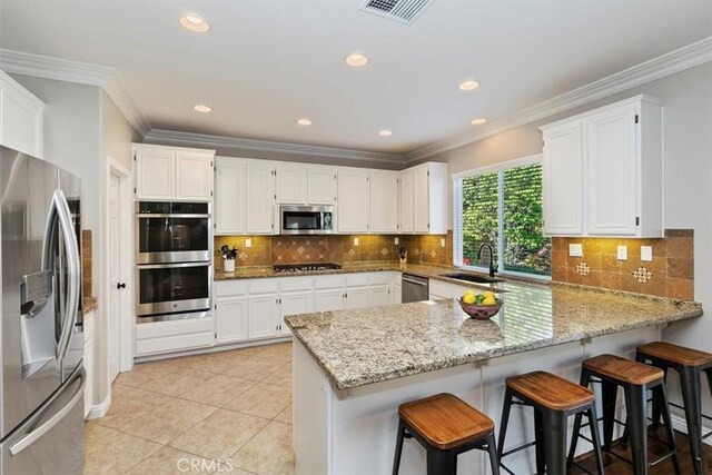 kitchen with appliances with stainless steel finishes, a sink, a peninsula, crown molding, and light stone countertops