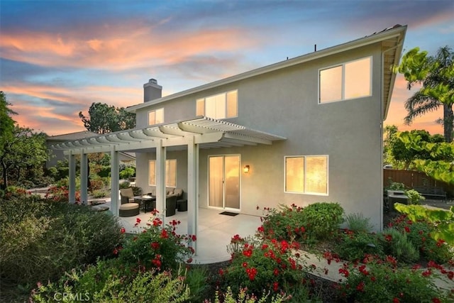 back of house at dusk with a pergola, a patio, a chimney, an outdoor living space, and stucco siding