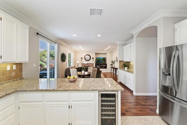 kitchen featuring stainless steel fridge with ice dispenser, wine cooler, a peninsula, backsplash, and white cabinetry