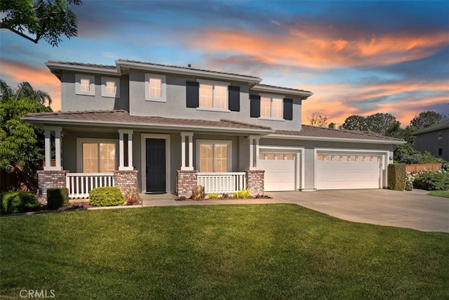 prairie-style home with covered porch, concrete driveway, stucco siding, a front yard, and an attached garage