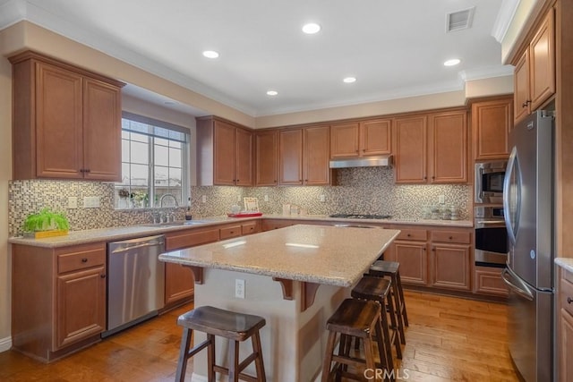 kitchen featuring stainless steel appliances, a sink, a kitchen breakfast bar, ornamental molding, and light wood-style flooring