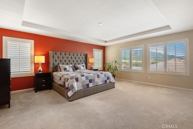 carpeted bedroom featuring a raised ceiling and baseboards