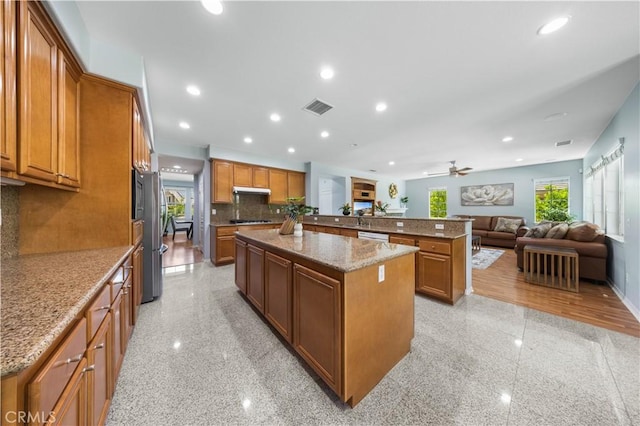 kitchen featuring brown cabinetry, a kitchen island, backsplash, granite floors, and open floor plan