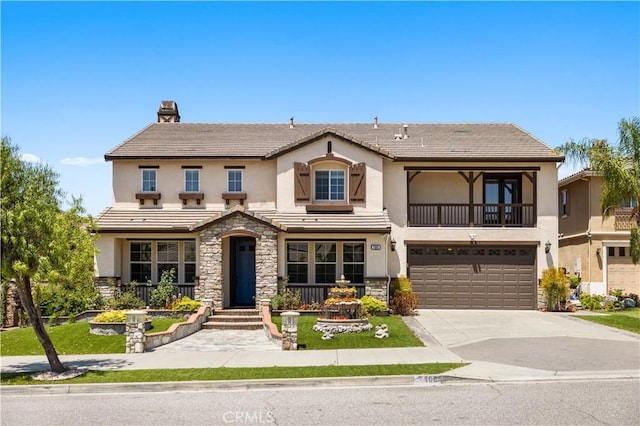 view of front of property with stucco siding, stone siding, an attached garage, a balcony, and driveway