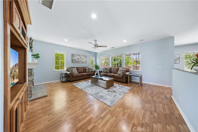 living room featuring ceiling fan, light wood-type flooring, baseboards, recessed lighting, and a fireplace