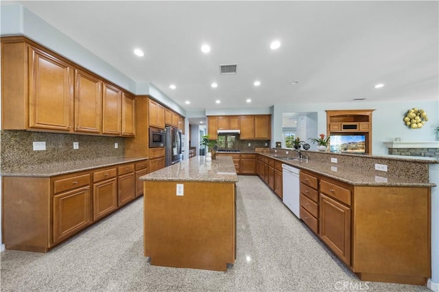 kitchen with appliances with stainless steel finishes, brown cabinets, light stone counters, under cabinet range hood, and a sink