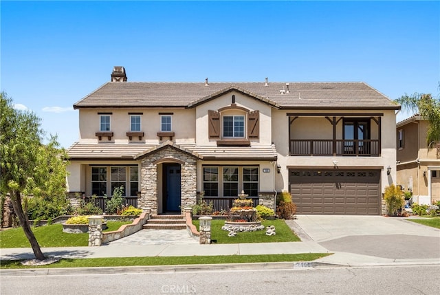 view of front facade featuring stucco siding, stone siding, a balcony, a garage, and concrete driveway