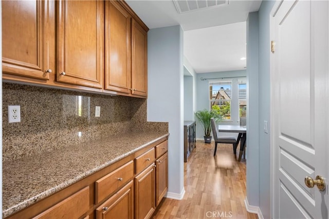 kitchen with brown cabinets, light wood-style flooring, tasteful backsplash, light stone counters, and baseboards