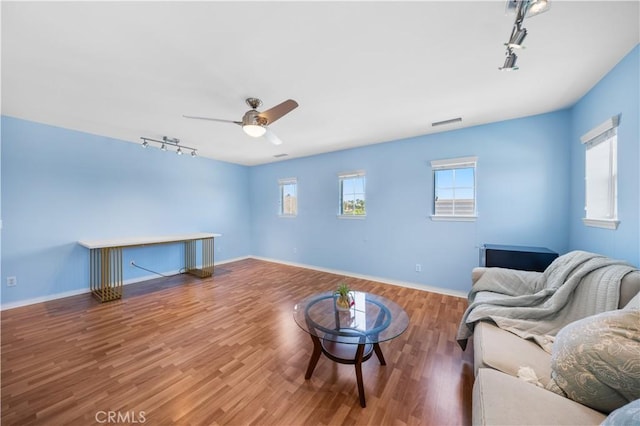 living room featuring track lighting, a ceiling fan, wood finished floors, and baseboards