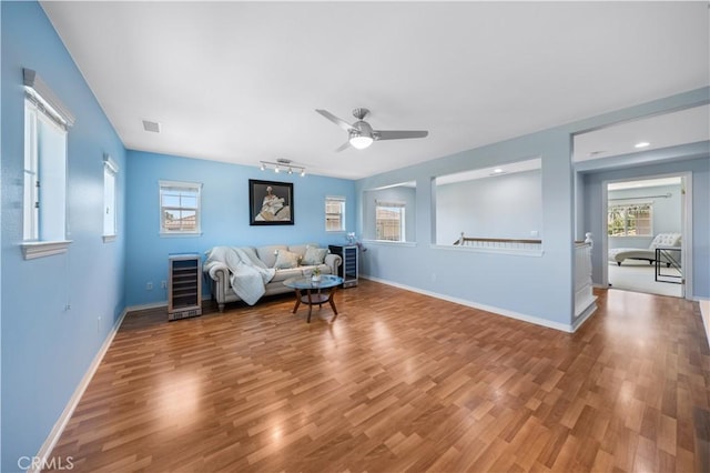 living area featuring beverage cooler, ceiling fan, wood finished floors, and baseboards