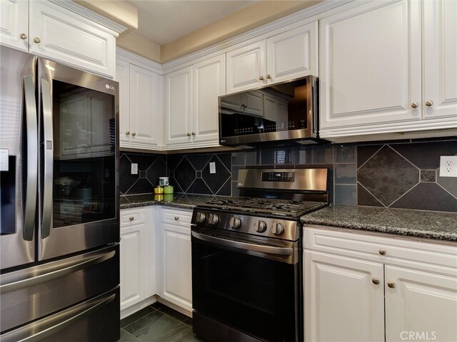 kitchen featuring stainless steel appliances, white cabinetry, decorative backsplash, and dark stone countertops