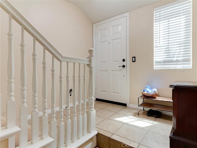 foyer entrance with light tile patterned flooring, lofted ceiling, and stairs