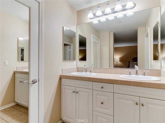 ensuite bathroom featuring double vanity, tile patterned floors, and baseboards