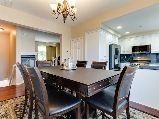 dining space with light wood-type flooring, a chandelier, a multi sided fireplace, and recessed lighting