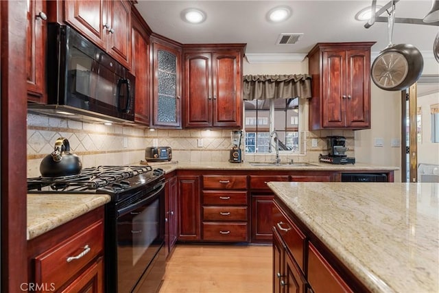 kitchen with black appliances, reddish brown cabinets, a sink, light stone countertops, and tasteful backsplash