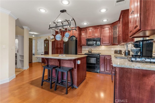 kitchen featuring black appliances, light wood-style flooring, a breakfast bar, ornamental molding, and backsplash