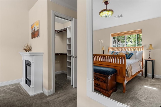 carpeted bedroom featuring baseboards, a spacious closet, and a glass covered fireplace