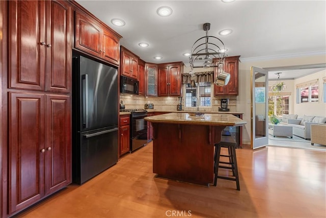 kitchen featuring black appliances, dark brown cabinets, a breakfast bar, crown molding, and tasteful backsplash