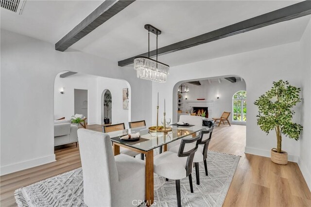 932 S Cloverdale Ave, Los Angeles, CA 90036 - dining space featuring arched walkways, beamed ceiling, light wood-style floors, baseboards, and a warm lit fireplace