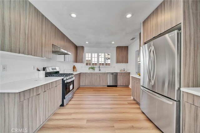 932 S Cloverdale Ave, Los Angeles, CA 90036 - kitchen featuring appliances with stainless steel finishes, modern cabinets, exhaust hood, a sink, and light wood finished floors