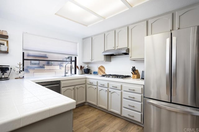 2506 Woodlands Way, Oceanside, CA 92054 - kitchen featuring stainless steel appliances, tile countertops, a sink, under cabinet range hood, and light wood finished floors
