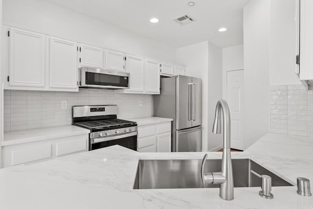 kitchen featuring stainless steel appliances, a sink, white cabinetry, light stone counters, and recessed lighting