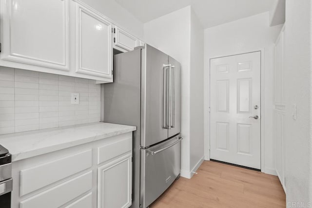 kitchen featuring freestanding refrigerator, white cabinetry, light wood-type flooring, backsplash, and light stone counters