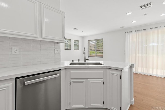 kitchen featuring stainless steel dishwasher, a sink, a peninsula, white cabinets, and backsplash