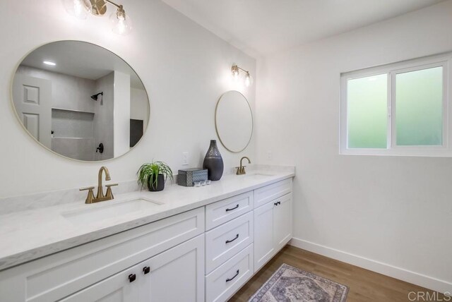 bathroom featuring double vanity, wood finished floors, baseboards, and a shower