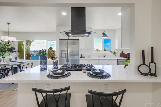 kitchen with stainless steel appliances, island range hood, a sink, white cabinets, and a kitchen breakfast bar