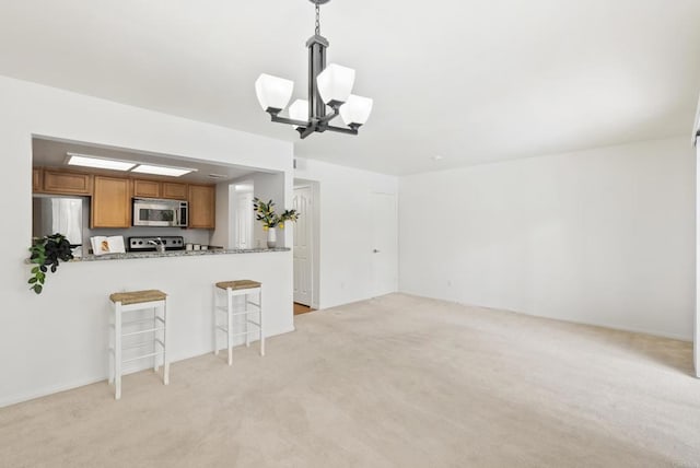 14936 Avenida Venusto Unit 12, San Diego, CA 92128 - kitchen with stainless steel appliances, brown cabinetry, a chandelier, light colored carpet, and a kitchen bar