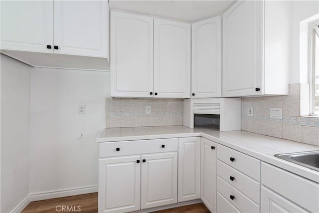 15821 Willett Ln, Huntington Beach, CA 92647 - kitchen featuring tasteful backsplash, white cabinets, baseboards, tile countertops, and wood finished floors