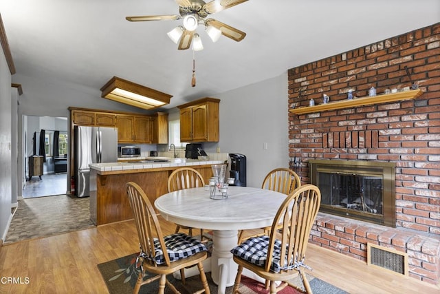 dining space with wood finished floors, vaulted ceiling, a ceiling fan, a fireplace, and plenty of natural light
