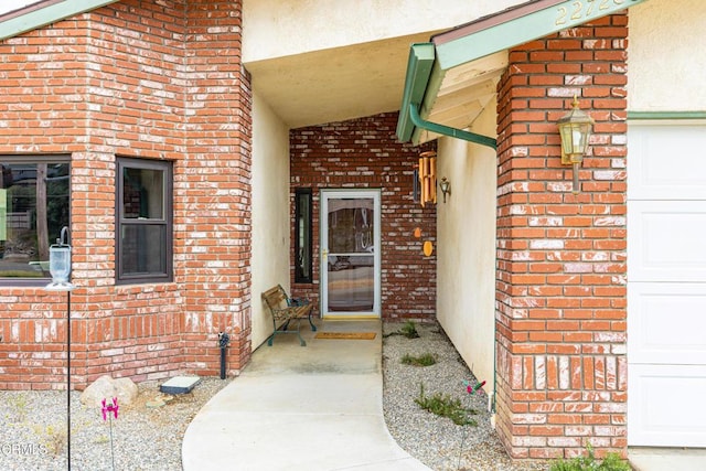 doorway to property with brick siding, an attached garage, and stucco siding