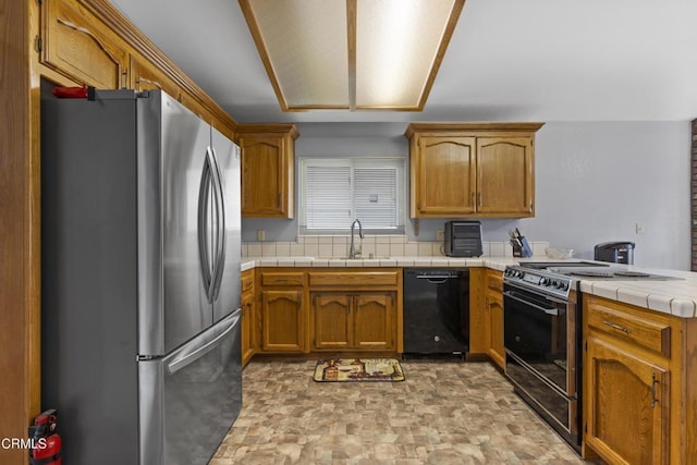 kitchen with stainless steel appliances, a sink, a peninsula, stone finish flooring, and brown cabinetry