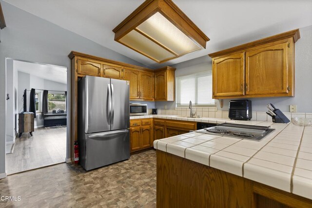 kitchen with appliances with stainless steel finishes, tile countertops, plenty of natural light, lofted ceiling, and brown cabinetry