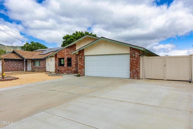 single story home with driveway, a gate, a garage, brick siding, and roof mounted solar panels
