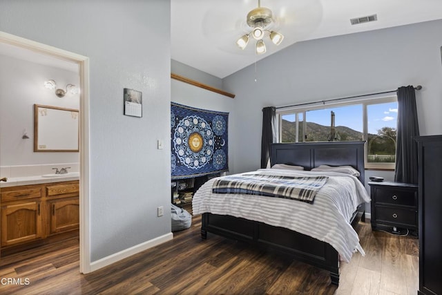 bedroom featuring lofted ceiling, wood finished floors, connected bathroom, baseboards, and a sink
