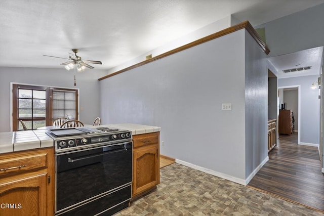 kitchen with black range with electric cooktop, tile counters, a ceiling fan, brown cabinetry, and baseboards