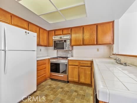 11255 Key W Ave Unit 2, Porter Ranch, CA 91326 - kitchen with freestanding refrigerator, stainless steel gas stove, tile counters, and brown cabinets