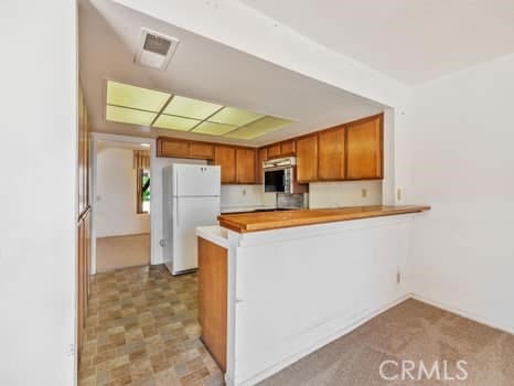 11255 Key W Ave Unit 2, Porter Ranch, CA 91326 - kitchen featuring freestanding refrigerator, stainless steel microwave, brown cabinetry, a peninsula, and light countertops