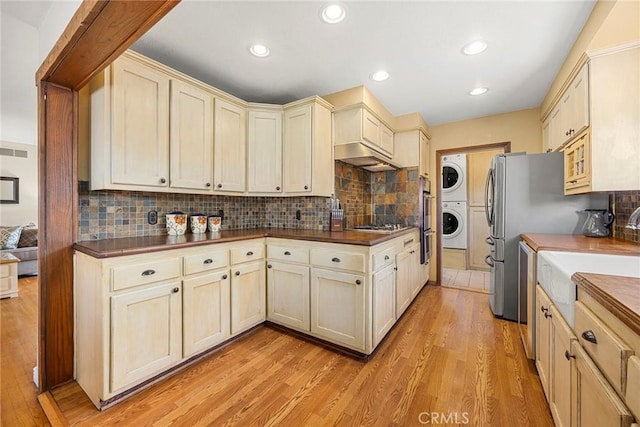 kitchen with estacked washer and dryer, dark countertops, a sink, light wood finished floors, and recessed lighting