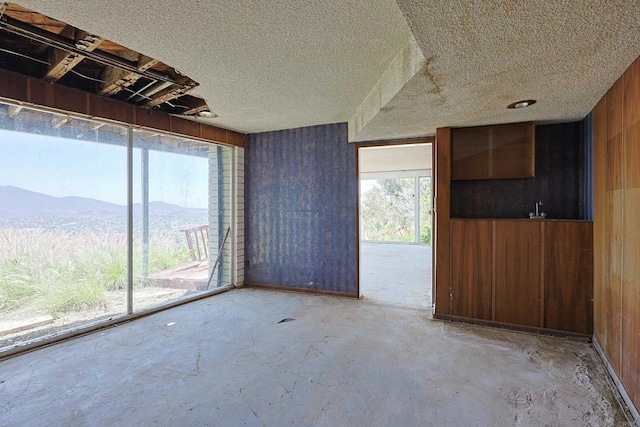 spare room featuring wooden walls, a mountain view, a textured ceiling, and unfinished concrete floors