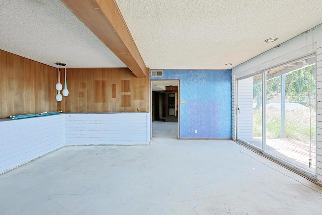 spare room featuring a textured ceiling, unfinished concrete flooring, and wood walls