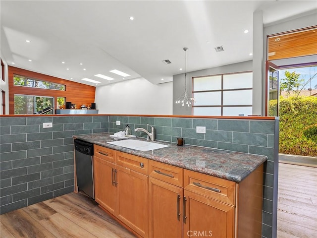 kitchen with stainless steel dishwasher, light wood-type flooring, tile walls, a sink, and dark stone countertops