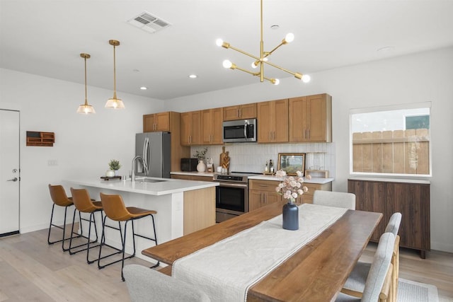 2210 Bonita Ct, Lemon Grove, CA 91945 - kitchen with appliances with stainless steel finishes, a kitchen island with sink, light wood-type flooring, decorative backsplash, and a sink