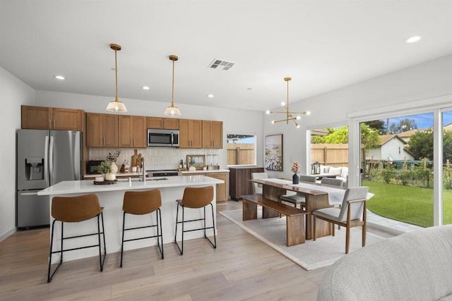 2210 Bonita Ct, Lemon Grove, CA 91945 - kitchen featuring appliances with stainless steel finishes, light countertops, decorative backsplash, brown cabinetry, and a kitchen island with sink
