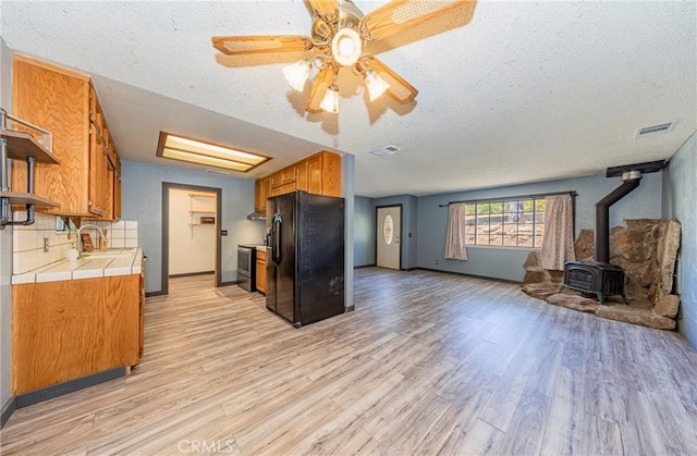 43096 Deer Trail Way, Coarsegold, CA 93614 - kitchen featuring black fridge with ice dispenser, tile countertops, a wood stove, open shelves, and light wood finished floors