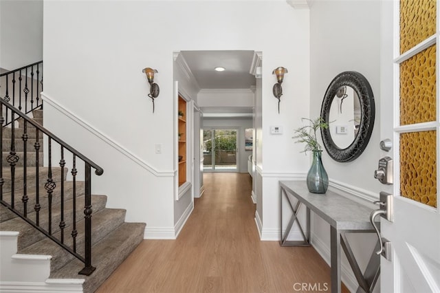 foyer with wood finished floors, ornamental molding, stairway, and baseboards
