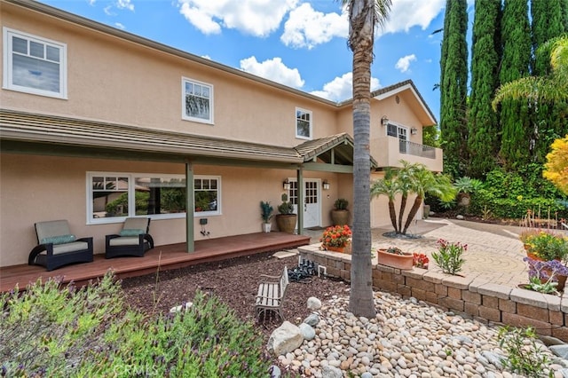 rear view of house featuring stucco siding, an attached garage, driveway, and a wooden deck